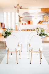 Elegant church wedding ceremony decoration with chairs adorned with white fabric, flowers, and ribbons, creating a romantic and festive atmosphere for the bride and groom