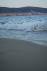 Soft sea waves washing sandy beach at sunset. Close-up seascape with gentle surf and golden light, symbol of calm, nature, and relaxation.