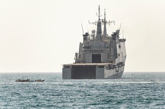 Military landing craft departs from the stern of a large naval ship