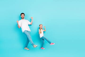 Happy father and adorable daughter dancing together on a bright turquoise background symbolizing...