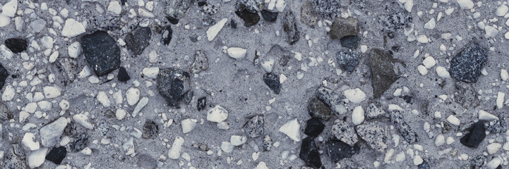 Concrete wall texture with pebbles. Decorative rough concrete surface with white, black and gray stones. Wide panoramic texture for background and design.