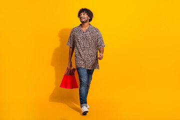 Smiling young man holding vibrant shopping bags on a bright yellow background showcasing fashion and casual style