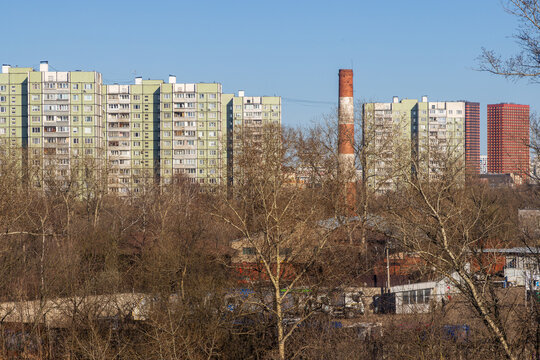 View of multi-storey panel residential buildings. In the foreground are trees and an industrial chimney. Residential area of the city.
