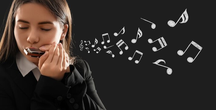 Young woman playing harmonica on dark background