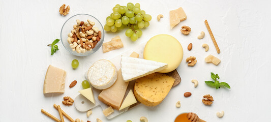 Board with different types of tasty cheese, grapes, nuts and honey on light background