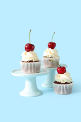 Stands with tasty cherry cupcakes on blue background