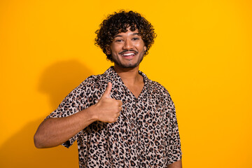 Confident young man in leopard print shirt giving thumbs up gesture against bright yellow background