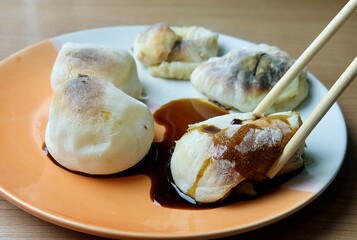 A pair of chopsticks lifts a hot grilled yakimochi, a beloved Japanese rice cake snack with a crispy exterior and chewy interior. It can be served sweet or savory.
