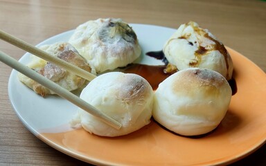 A pair of chopsticks dips a hot, grilled yakimochi into a small bowl of savory soy sauce, creating a delicious and popular traditional Japanese snack.