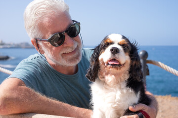 Carefree senior man sitting on a bench close to the beach with his cavalier king charles dog. Best friend forever concept