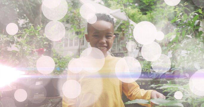 Smiling child wearing yellow shirt standing in backyard garden, with potted plants and umbrella