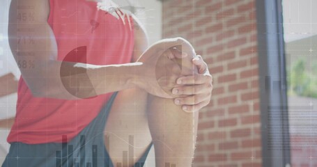 Grasping opposite knee while kneeling in gym area, wearing red sportswear with floating data charts