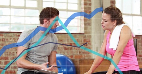 Holding clipboard instructor discussing workout with client in studio, cardio machine, towel