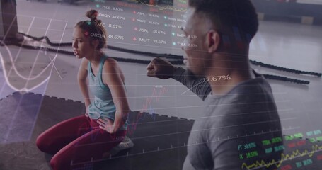 Gray-clad trainer guiding kneeling trainee in red leggings on black mats at gym with battle ropes