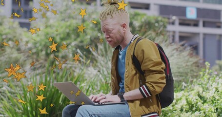 Working albino man wearing mustard jacket typing on laptop in park, with star overlays, copy space