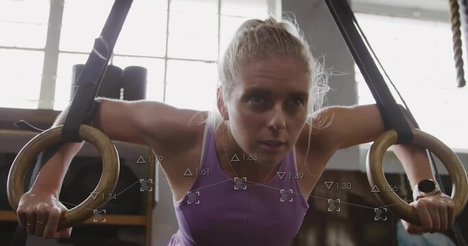 Leaning woman gripping wooden rings on suspension straps in gym, wearing purple top and smartwatch