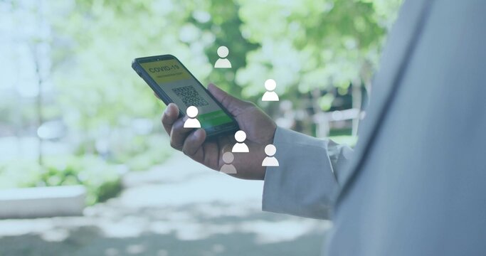 Man in coat holding phone viewing COVID QR code in sunlit garden path, with floating icons - Powered by Adobe