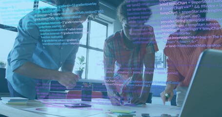 Collaborating software developers reviewing code on laptop at office desk, with pens, code overlay