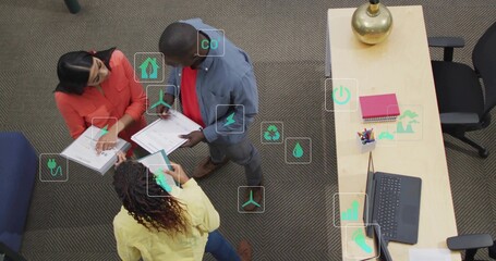 Office professionals discussing sustainability on carpeted floor with documents tablet and laptop