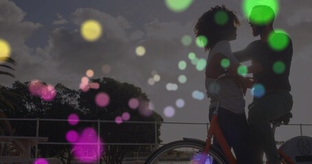 Leaning couple holding bicycle on waterfront by metal railing at sunset with bokeh, copy space