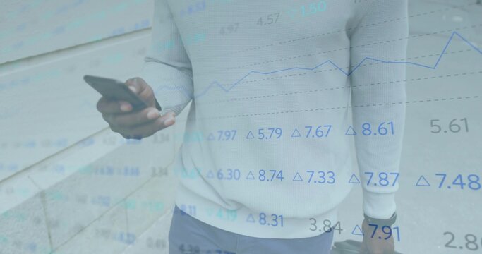 Holding smartphone and gripping suitcase, businessman standing at stone wall with financial overlay