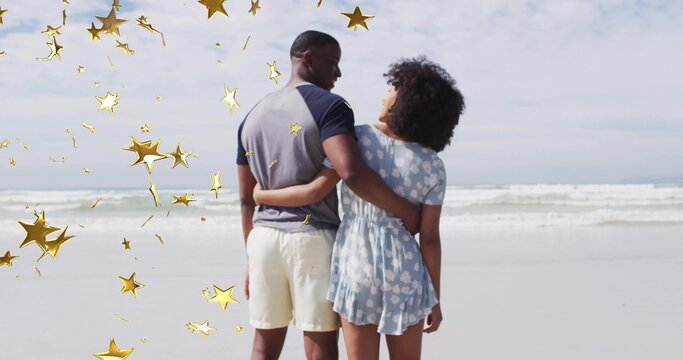 Standing adult couple holding waists at sandy beach shoreline, with decorative golden star shapes - Powered by Adobe