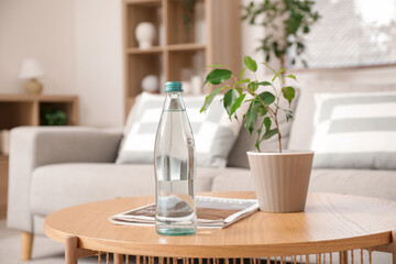 Bottle of water with magazine and plant on table in living room, closeup
