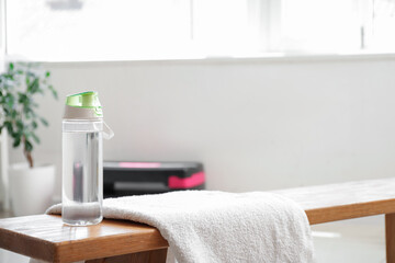 Sports water bottle with towel on bench in gym, closeup
