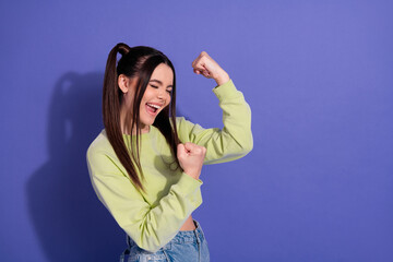 Cheerful young woman celebrating success with enthusiastic gestures against vibrant purple...
