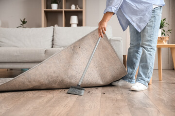 Woman swiping floor under carpet at home