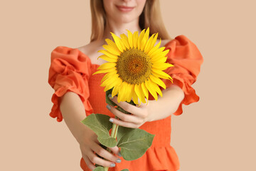 Beautiful young happy woman with sunflower on beige background, closeup