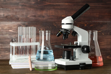 Modern microscope with chemical flasks on table against wooden background
