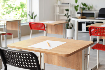 Sheet of paper and pencil on desk in empty classroom. Closeup