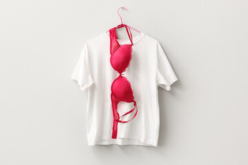 Red female bra and t-shirt hanging on light wall