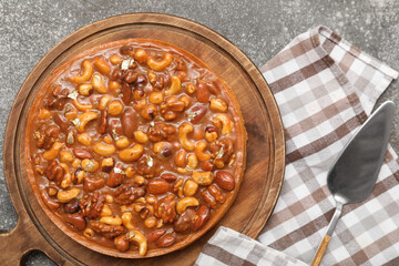 Wooden board of sweet tart with different nuts and caramel on grey background