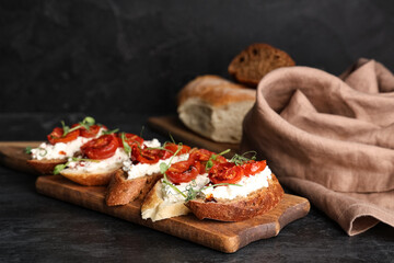Wooden board of tasty tomato bruschetta with ricotta on black background