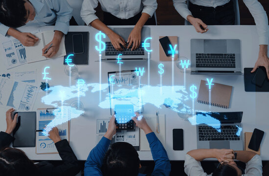 A diverse business team engages in strategic financial discussions while analyzing data and interacting with virtual currency icons representing the global economy. Trope