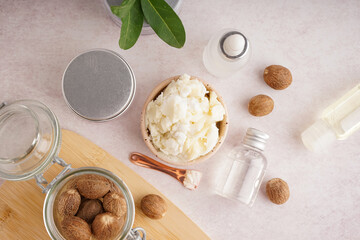 Composition with bowl of shea butter, nuts and cosmetic products on light background
