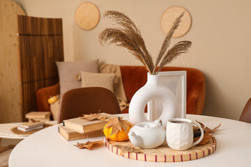 Table with hot tea, poppy buns, pampas grass and autumn leaves in living room