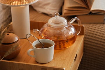 Teapot, cup of tea and lamp on bedside table in bedroom. Closeup