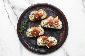 Plate of delicious fig bruschetta with ricotta and blue cheese on white background