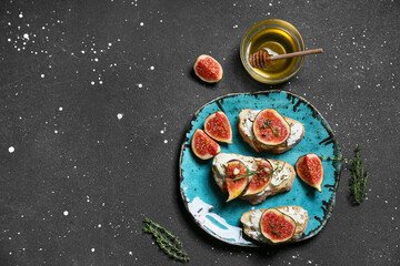 Plate of delicious fig bruschetta with ricotta cheese and bowl of honey on black background