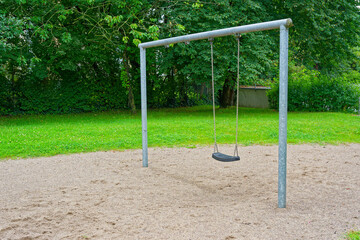 Fototapeta premium Playground swing frame with one black seat and green lawn