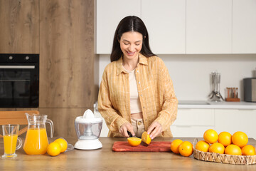 Young woman cutting fresh oranges in kitchen