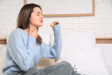Ill young woman taking cough syrup in bedroom