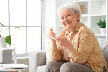 Senior woman with cup of butterfly pea flower tea sitting on sofa in living room