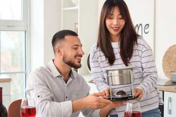 Young happy woman bringing cheese fondue for snacks and glasses of wine to her boyfriend at home
