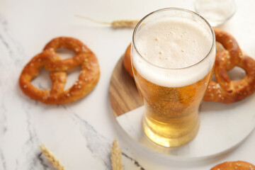 Board with glass of beer and pretzels on marble background, closeup