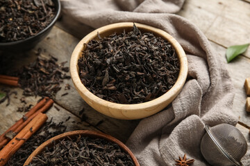 Bowls with dry black tea leaves and cinnamon on wooden background, closeup