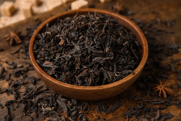 Bowl with dry black tea leaves and star anise on wooden background, closeup